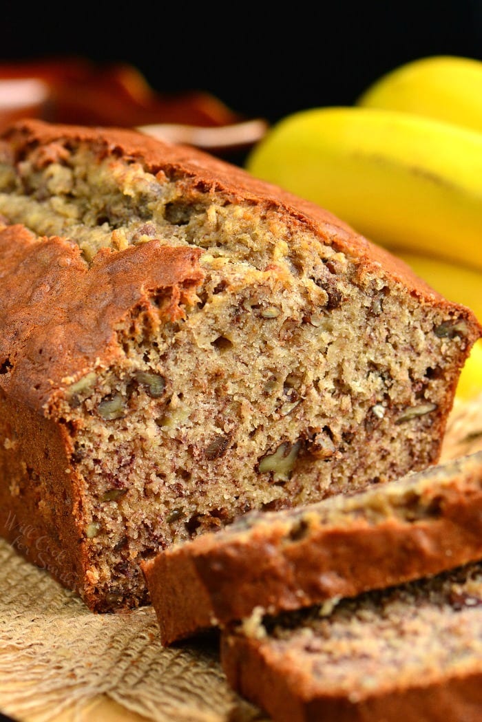 Banana Bread with two slices on a burlap placemat and banana's in the background 