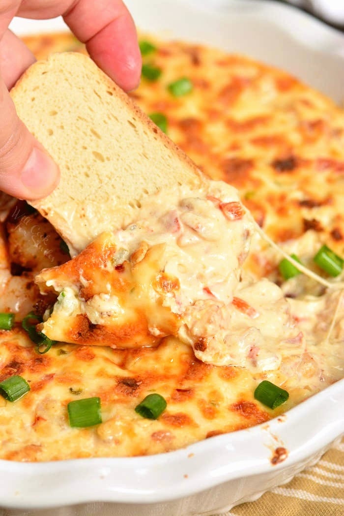 Shrimp Dip in a baking dish with crusty bread dipping some out 