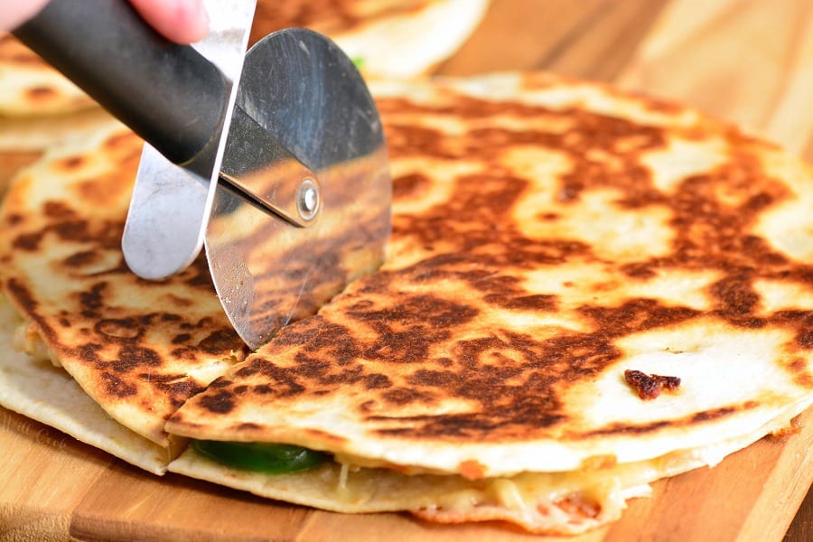 cutting quesadilla with a pizza cutter on a wood cutting board.