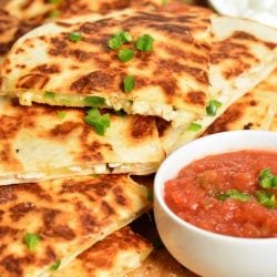 horizonal photo of chicken quesadilla with a small bowl of salsa.