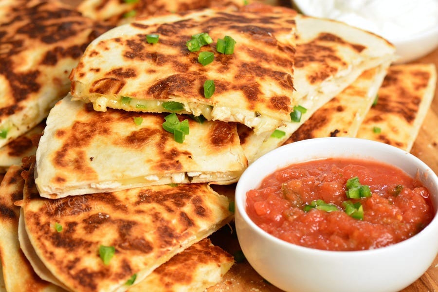 horizonal photo of chicken quesadilla with a small bowl of salsa. 