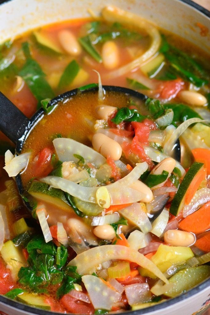 ladling out minestrone soup out of the pot.