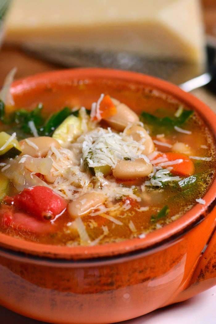 side view of minestrone soup in a red bowl.