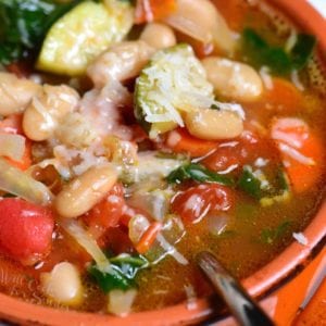 closeup of a red bowl with minestrone soup with a spoon.