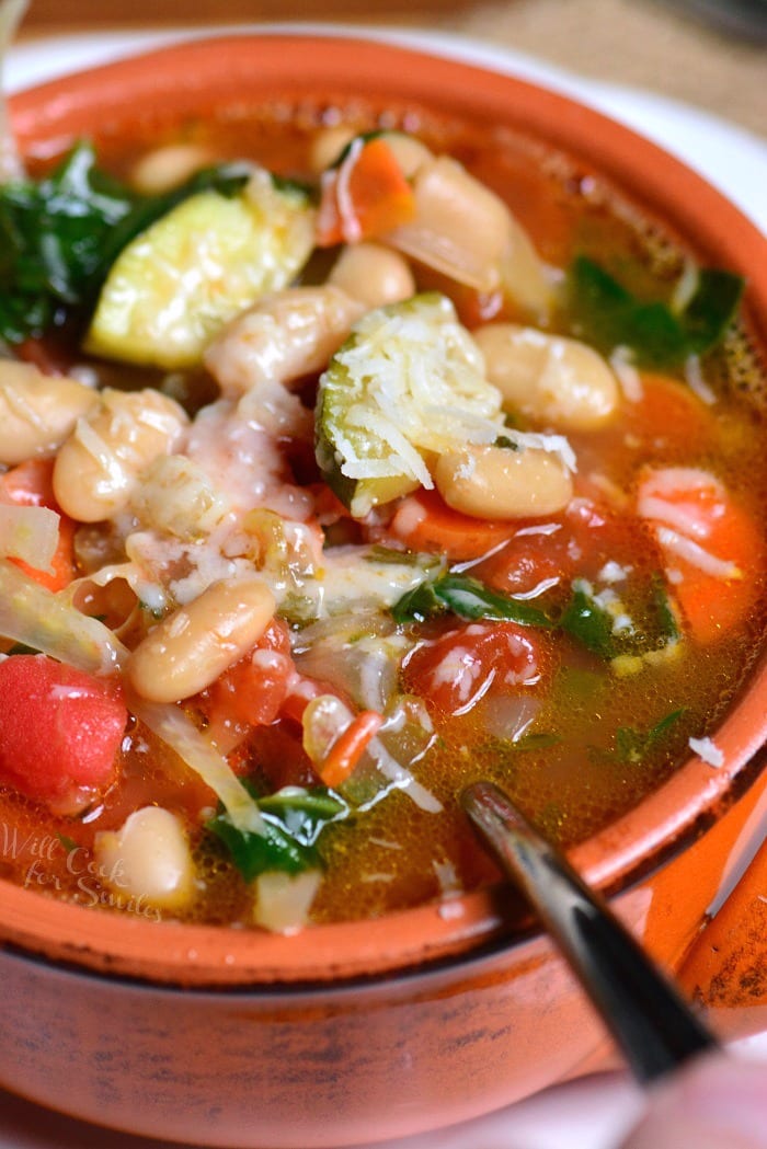 closeup of a red bowl with minestrone soup with a spoon.