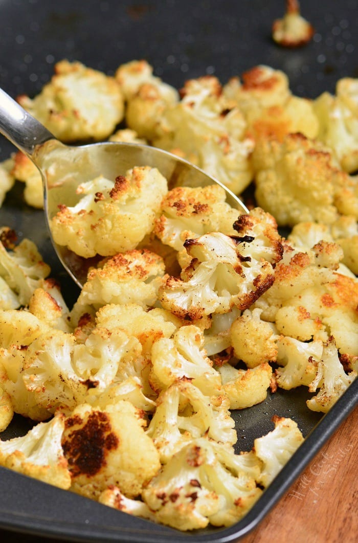 Roasted cauliflower on a baking sheet with a metal serving spoon 