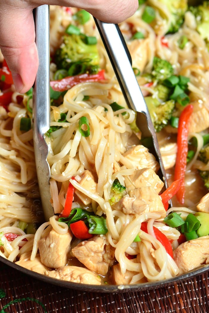 Sesame Chicken with Noodles in a pan lifting some out with tongs 