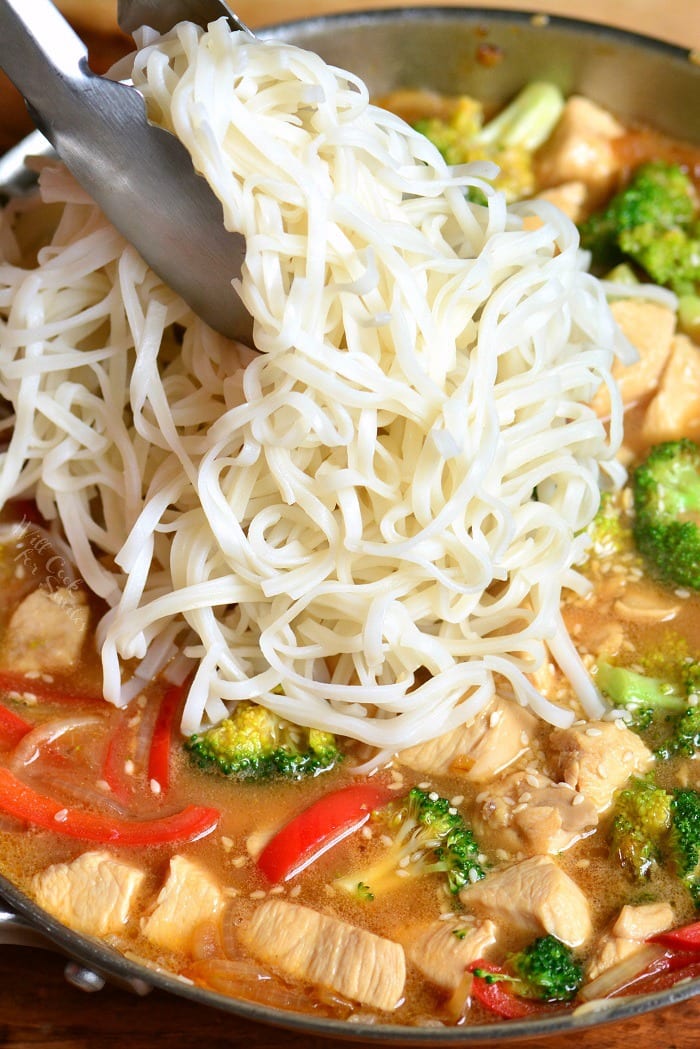 adding noodles to Sesame Chicken in a pan 