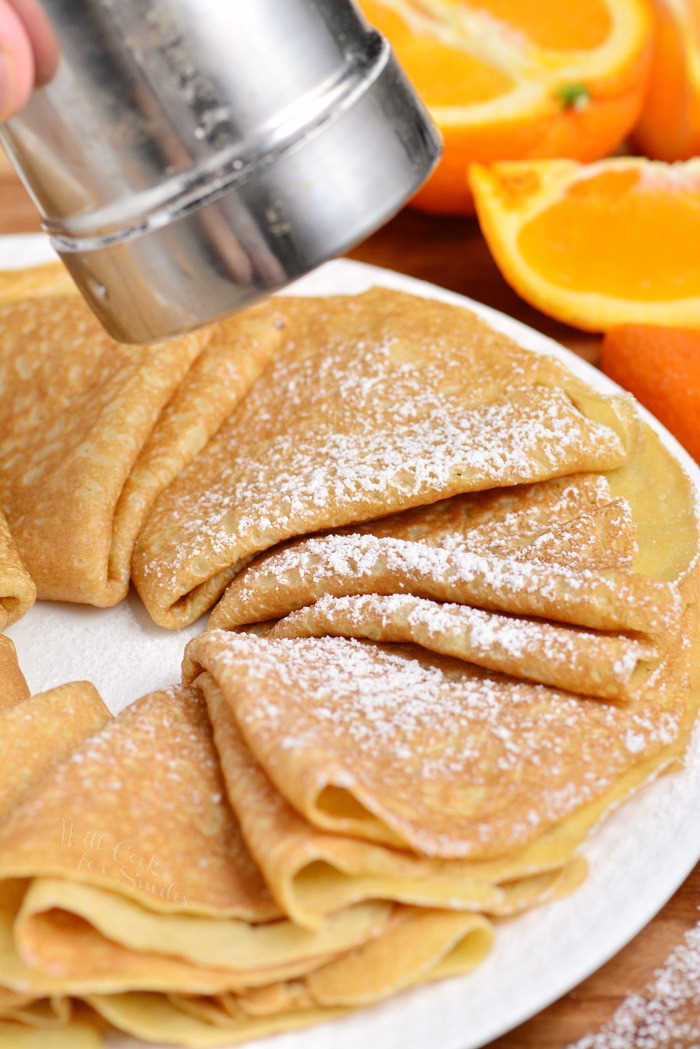 crepes on a plate with powdered sugar being poured on top.