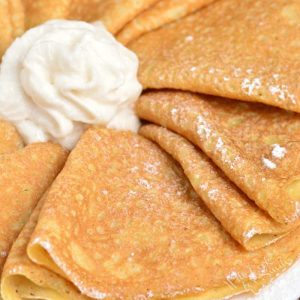 Crepes folded up on a plate with whipped cream in the middle.