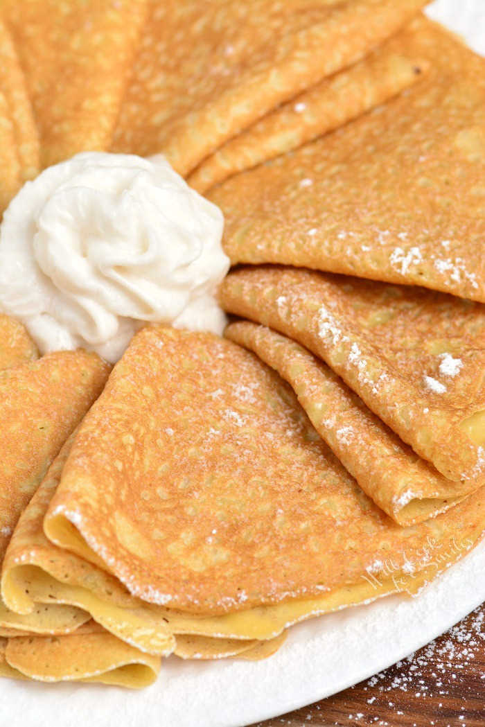 Crepes folded up on a plate with whipped cream in the middle.