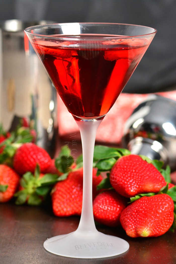 Strawberry Shortcake Martini in a martini in a martini glass on a wood table with strawberries around it 