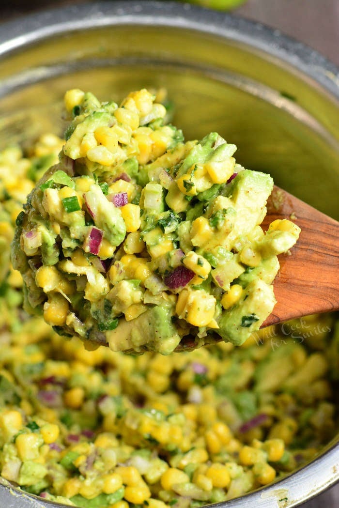 Corn Salad in a metal bowl scooping some out with a wooden spoon 