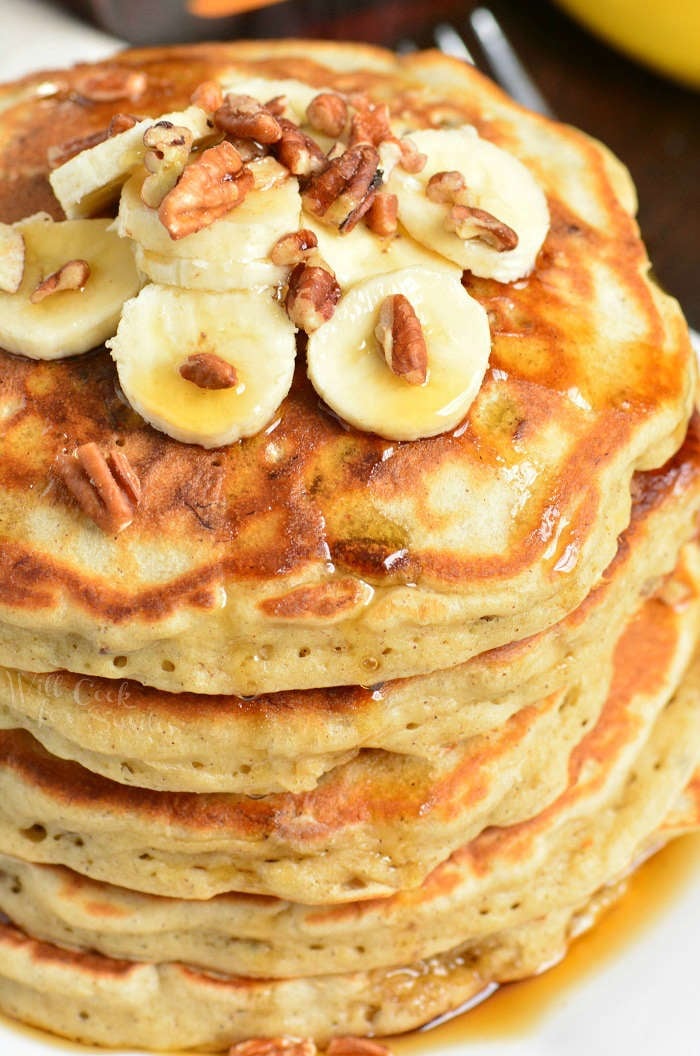 Banana Pancakes stacked on a plate with banana's, syrup, and nuts on top