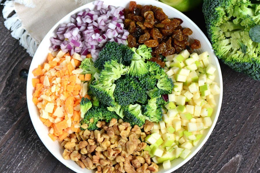 ingredients for broccoli salad in a serving bowl on a wooden cutting board 