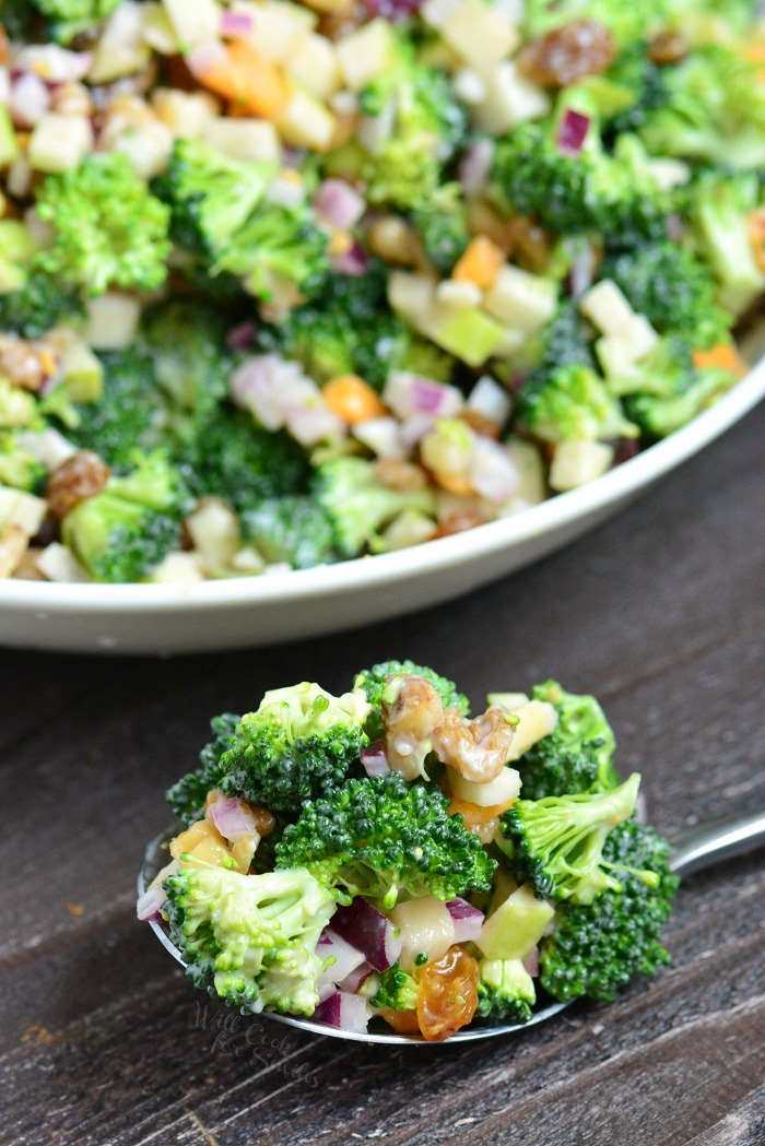 The BEST Broccoli Salad in a serving bowl with a spoon full of salad in front of it on a wood cutting board 