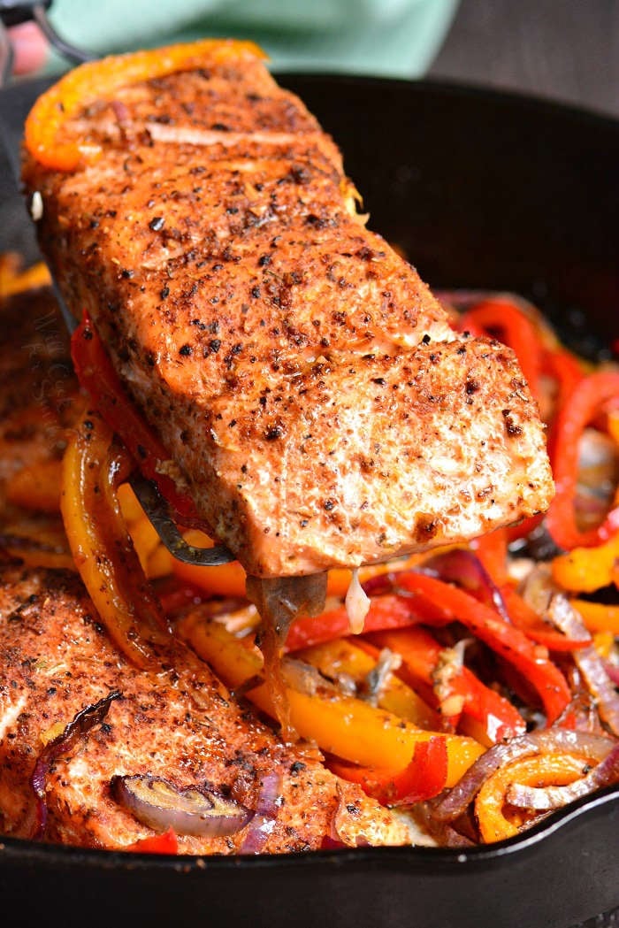 lifting cajun baked salmon out of cast iron pan with a spatula 