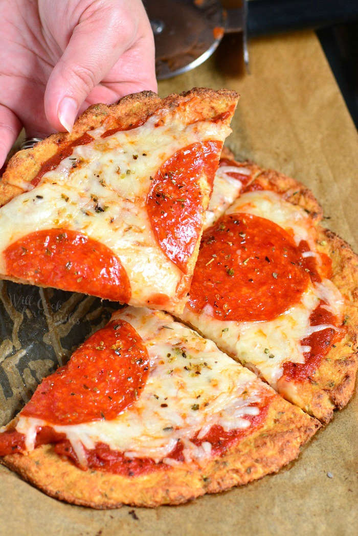 Cauliflower Pizza Crust pepperoni pizza on parchment paper with me holding a slice 