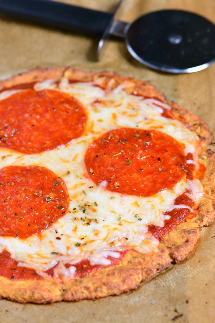 Cauliflower Pizza Crust pepperoni pizza un sliced on parchment paper with pizza cutter 