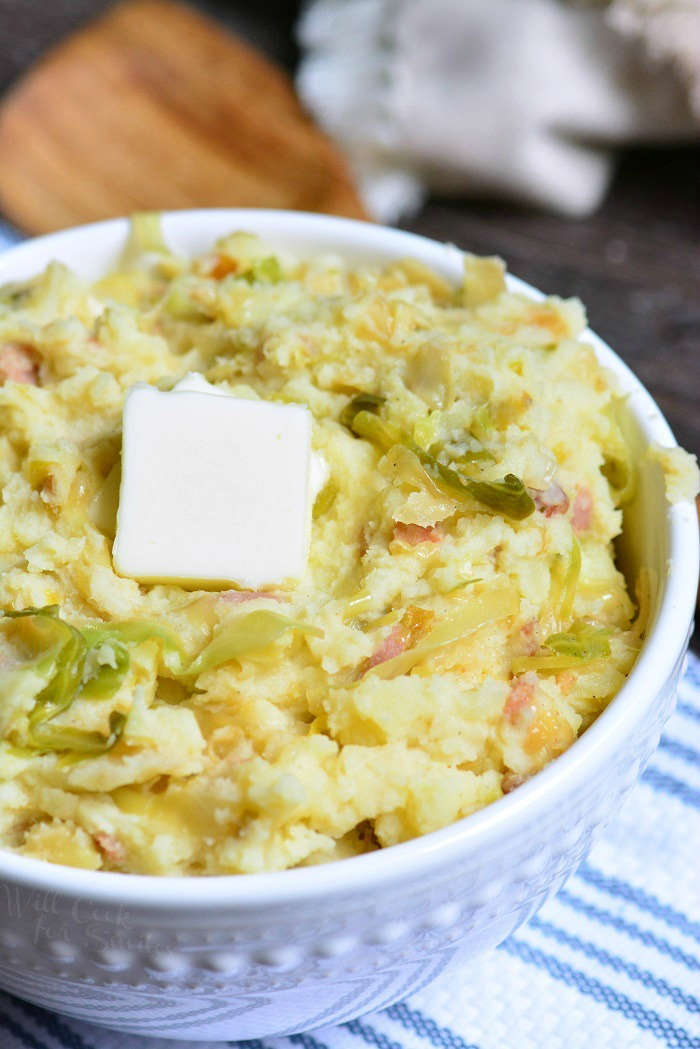 Colcannon in serving bowl with pats of butter on top sitting on a blue and white towel 