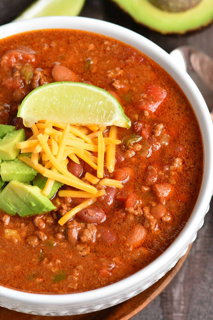 Instant Pot Chili in a bowl with a wedge of lime, cheese, and avocado on top 