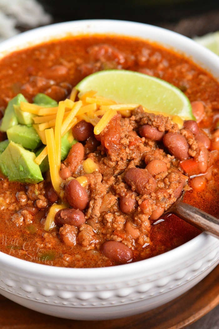 Instant Pot Chili in a bowl with cheese, lime wedge and avocado on top. with a spoon scooping out chili 