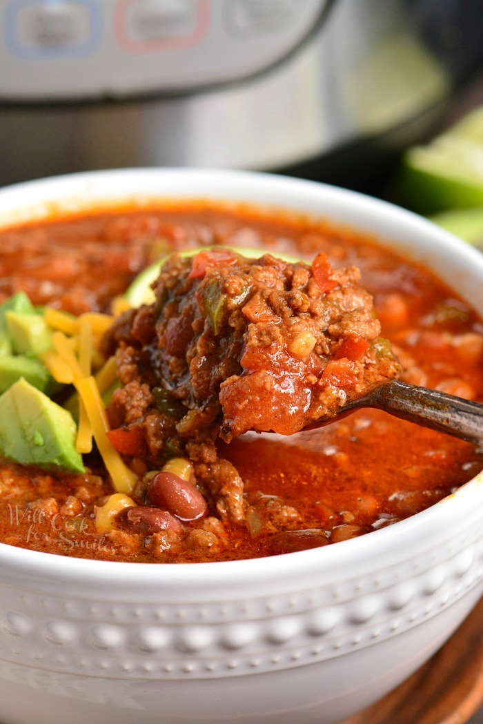 Instant Pot Chili in a bowl with cheese, lime wedge and avocado on top. with a spoon scooping out chili 