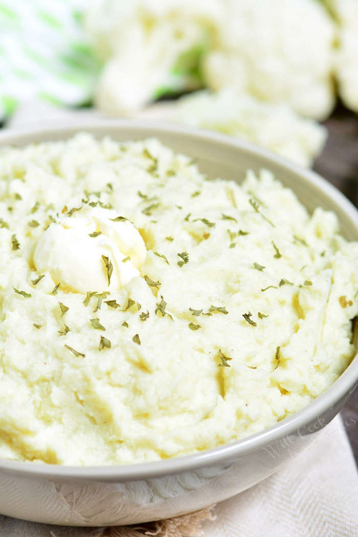 Mashed Cauliflower in a serving bowl with butter and herbs 