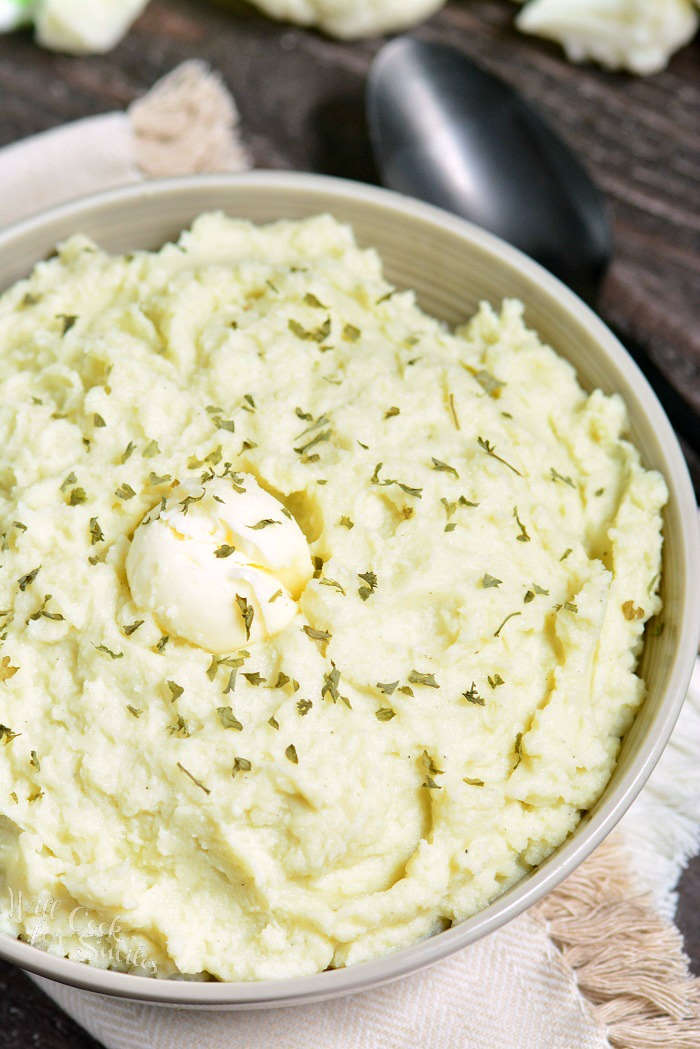 Mashed Cauliflower in a serving bowl with herbs and butter over top 