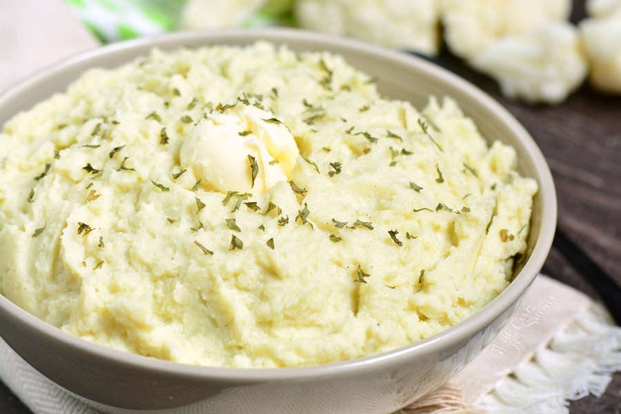 Mashed Cauliflower in a serving bowl with butter and herbs 
