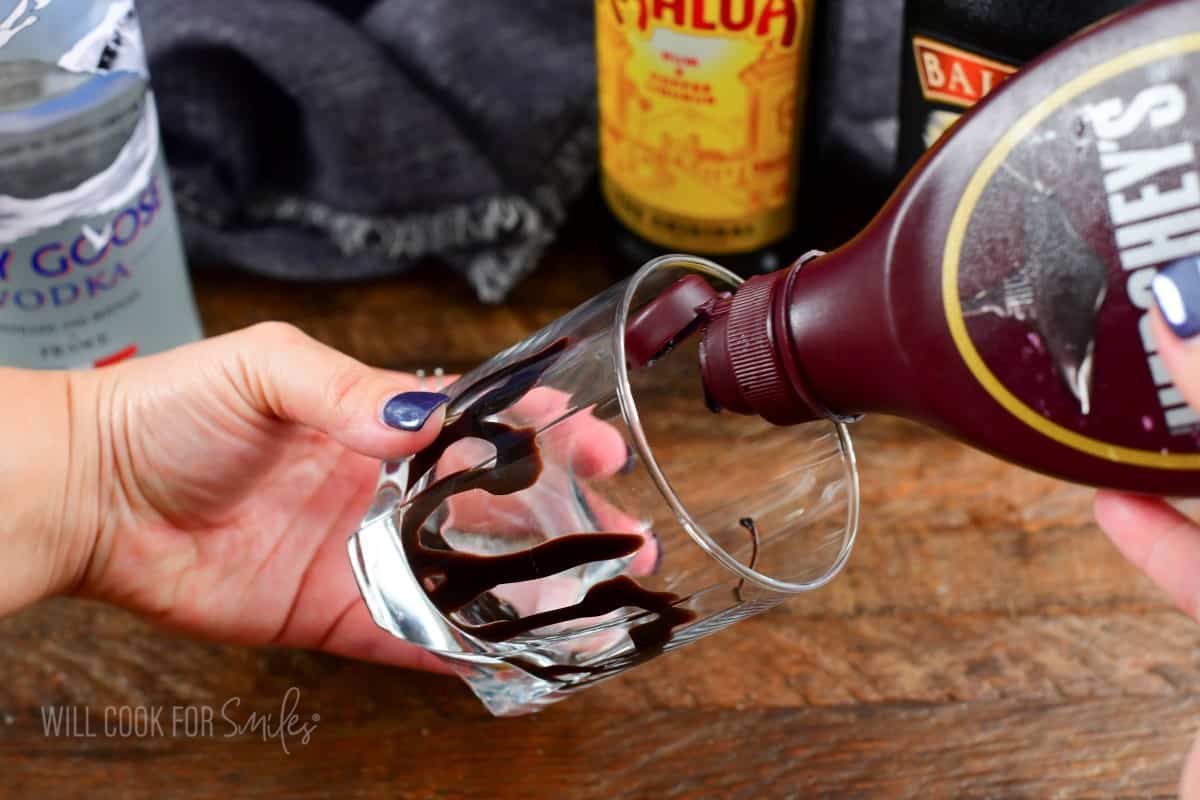 drizzling chocolate syrup into a rocks glass to decorate it.