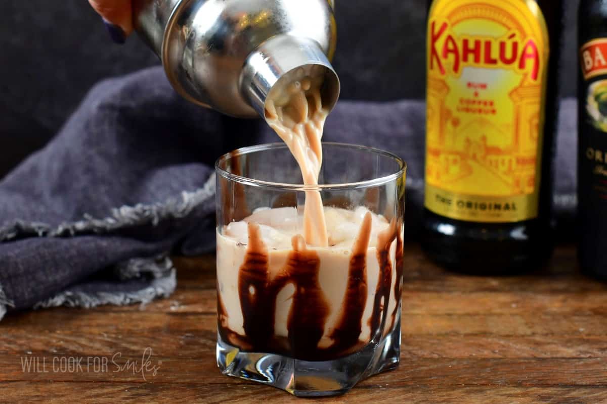 pouring creamy mudslide cocktail into the rocks glass with ice.