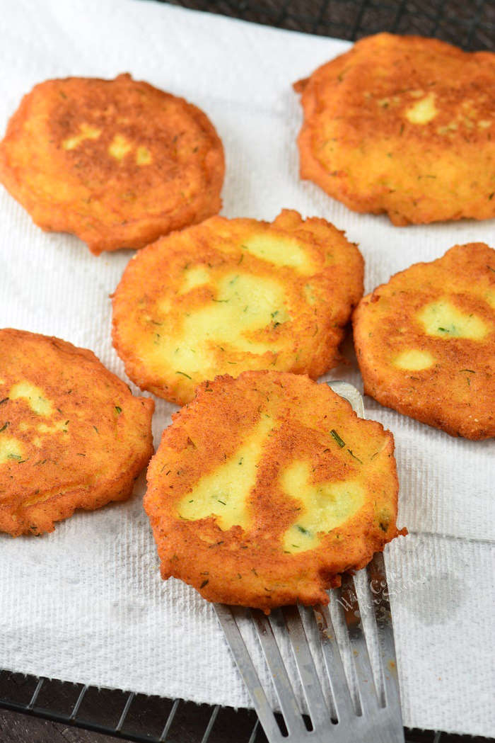 potato pancakes on a paper towel with a spatula and one pancake on it.