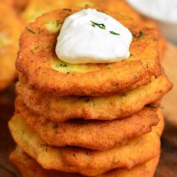 above shot of potato pancakes with a dollop of sour cream on top on a wood cutting board.