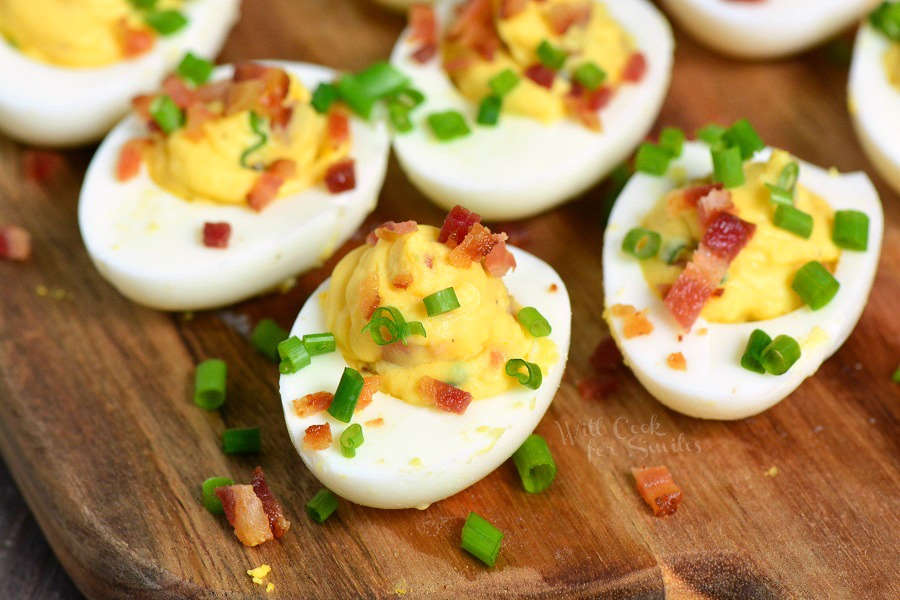 Classic Deviled Eggs with bacon and chives on top sitting on wood cutting board  