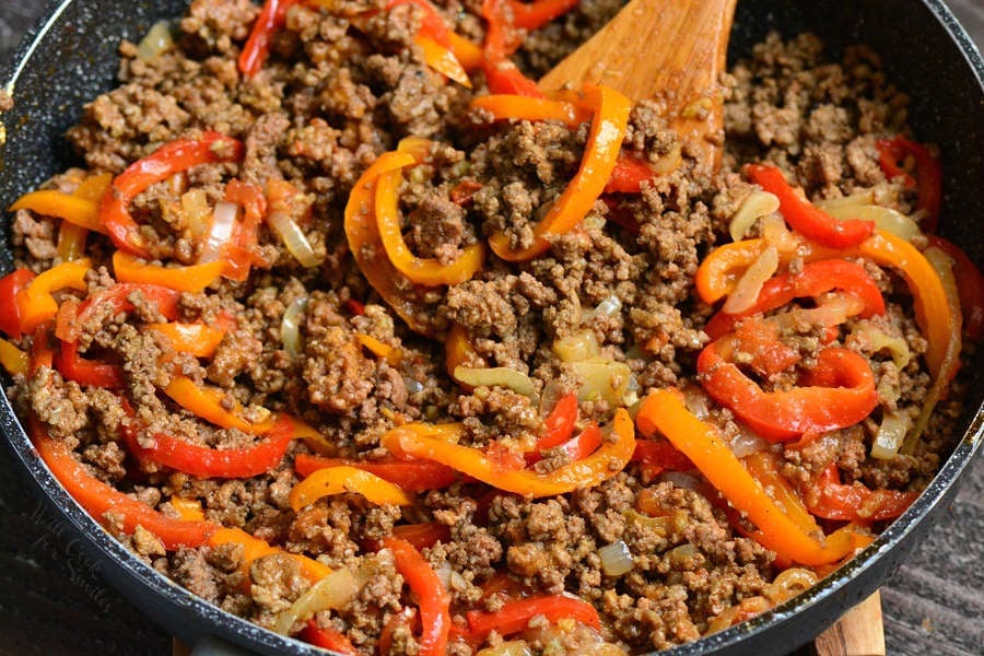 Beef, onions, and peppers, enchiladas in a pan being stirred by wooden spoon 