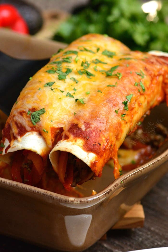 Beef Enchiladas being lifted out of casserole dish 