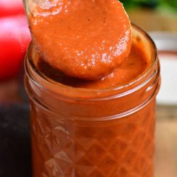 scooping out some enchilada sauce with a wooden spoon from a jar.