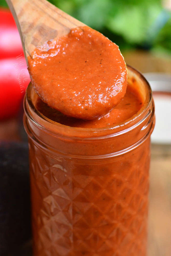 scooping out some enchilada sauce with a wooden spoon from a jar.