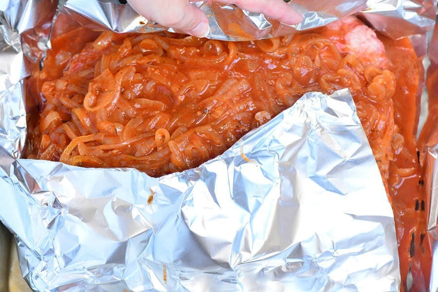 beef brisket in the oven being wrapped in tin foil 
