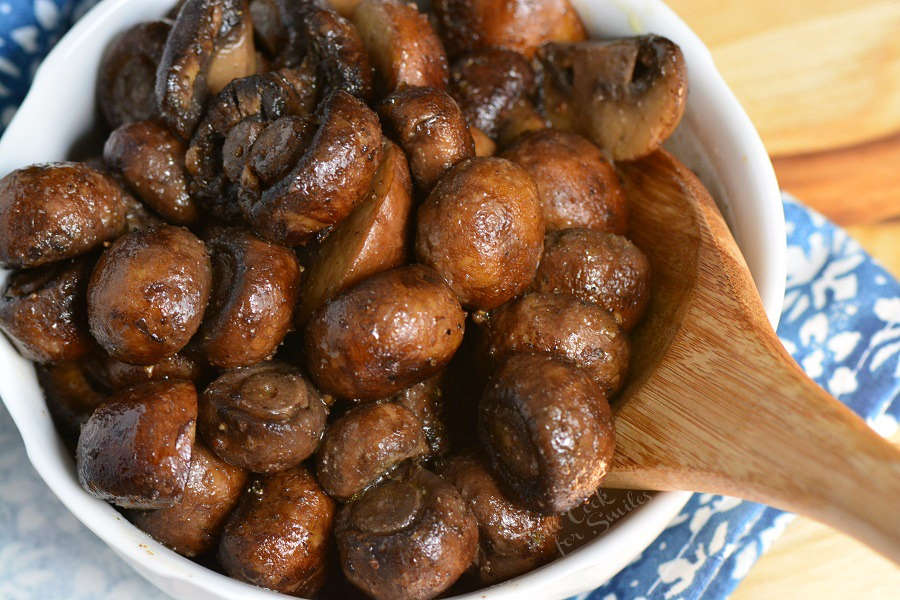 cooked mushrooms in a white bowl with a wooden spoon on a cutting board