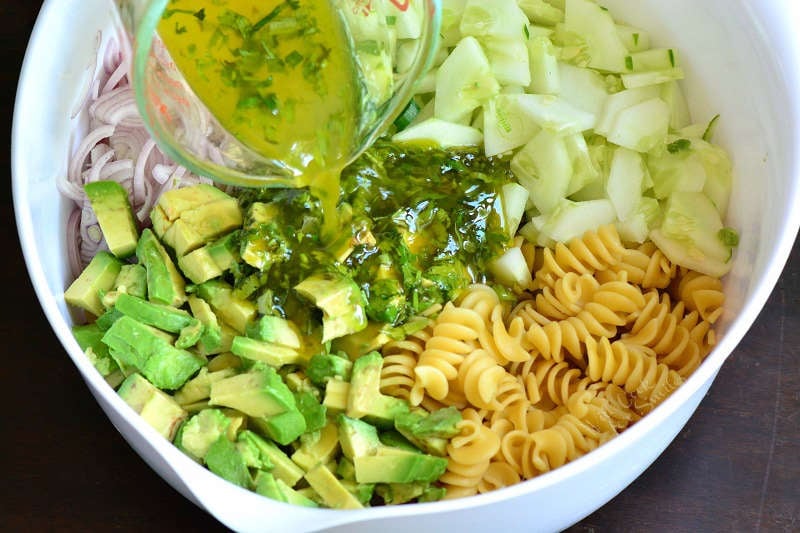 cilantro lime dressing being poured into avocado pasta salad 