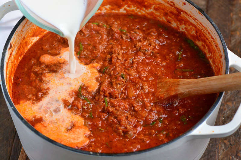 pouring cream into sauce that is in a pan 