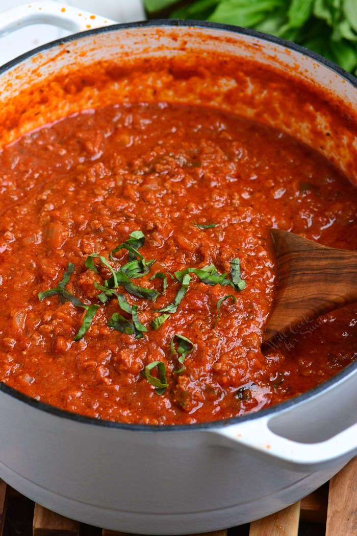 Bolognese Sauce in a stock pot with a wooden spoon on a wood cutting board 