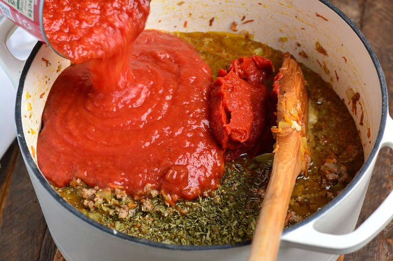 pouring tomato into a stock pot with other ingredients 