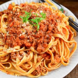 fettuccine pasta mixed and topped with a tomato based meat sauce on a plate.