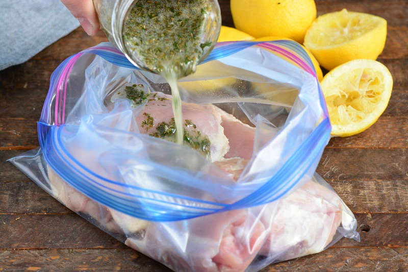 pouting chicken marinade in a ziplock bag with chicken drum sticks, bag is sitting on a wood cutting board with lemon 