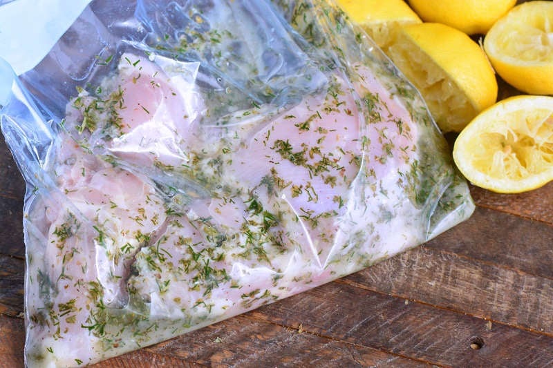 Marinading Greek Chicken in a ziplock bag that is on a wood cutting board with lemons 