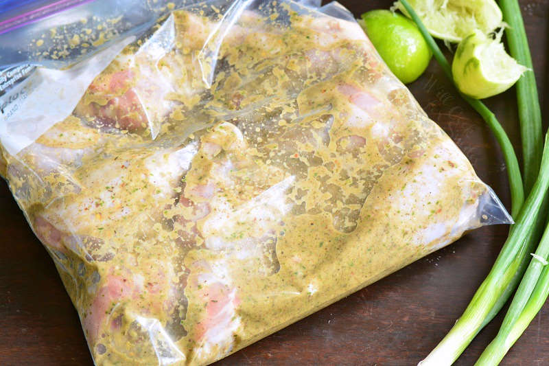 Marinating Jerk Chicken in a ziplock bag on a wood cutting board with a lime and chives