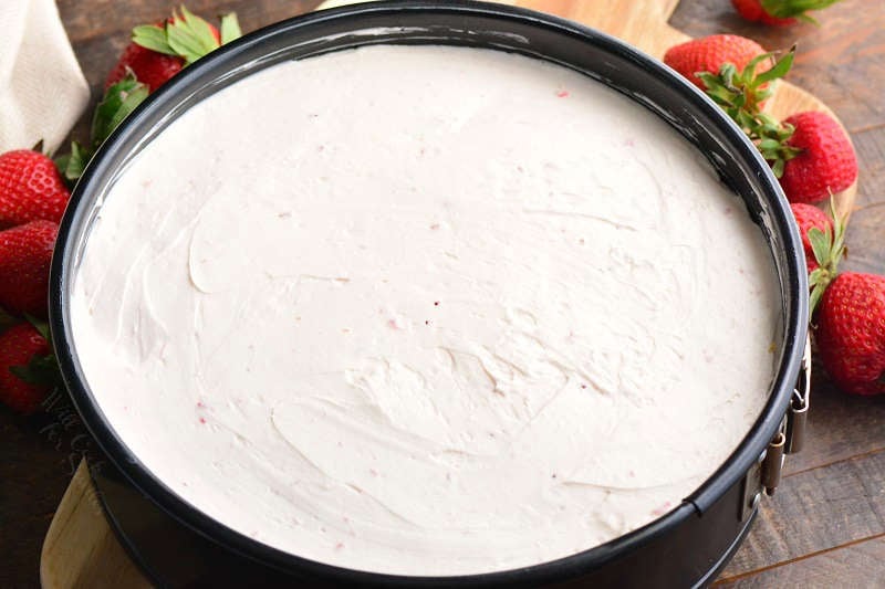 no bake cheesecake in a spring form pan on a wood cutting board with strawberries around it